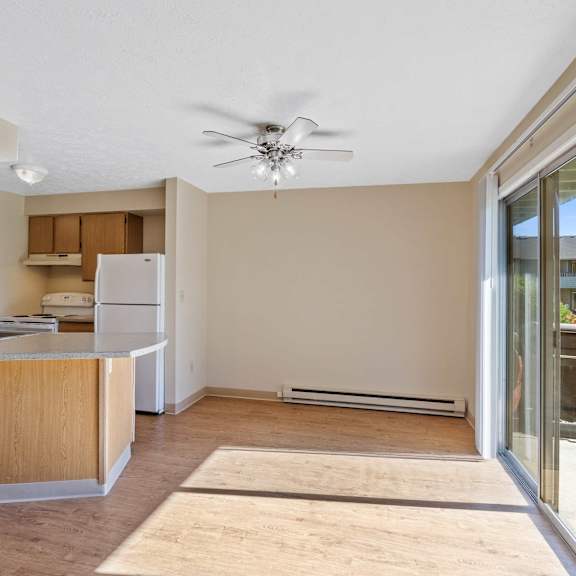an empty living room with a kitchen and a ceiling fan