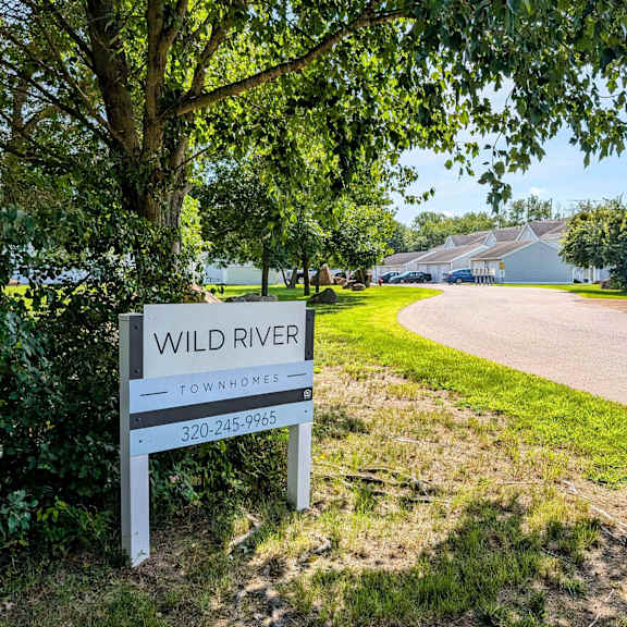 a sign for the wild river subdivision in front of a road and a tree