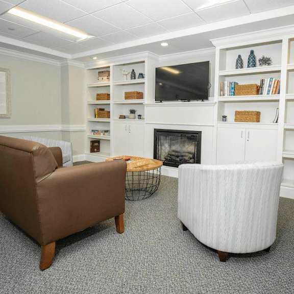 a living room with a brown chair, a white chair, and a fireplace.