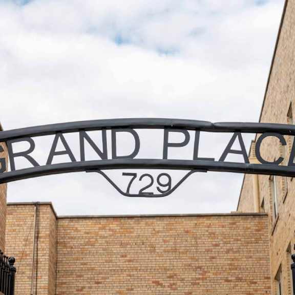 a sign that says grand place 729 is hanging from a black metal frame.