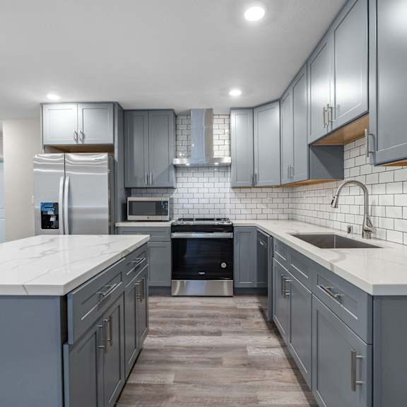an open kitchen with gray cabinets and white counter tops and a sink