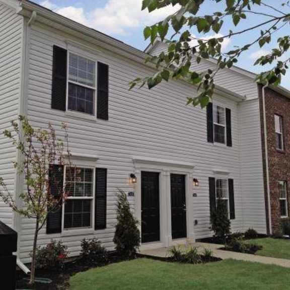 a white house with black shutters and a brick building next to it.