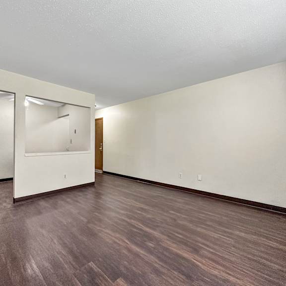a room with a wooden floor and a white wall with a mirror and a door.