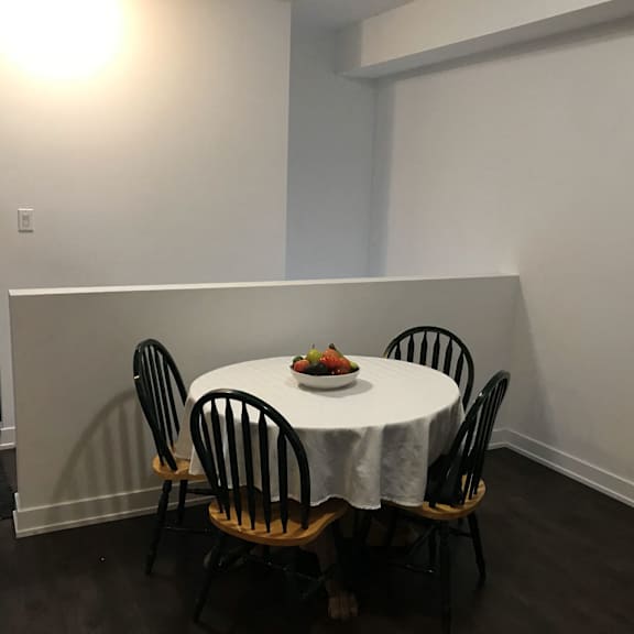 a table with a white cloth and a bowl of fruit on it is surrounded by four chairs.