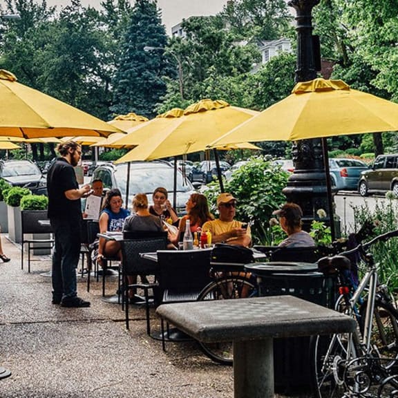 people sitting at tables with yellow umbrellas on a sidewalk