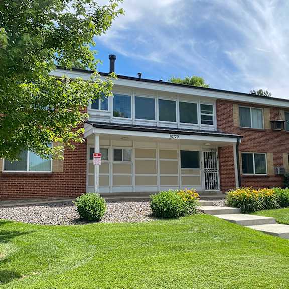 2-story red brick building with concrete steps leading to entry, landscaping and trees.