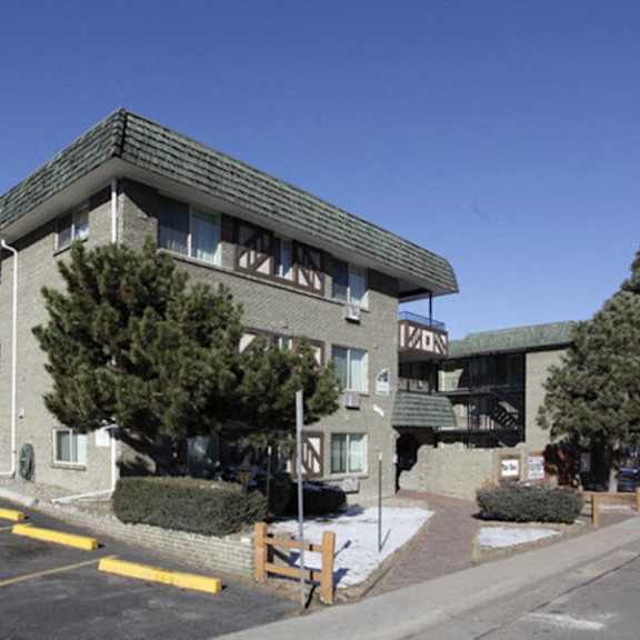 a building with a green roof and a sign that reads "12.30" is surrounded by trees and a parking lot.