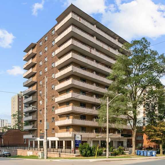 a large brown building with many windows and balconies is surrounded by trees and a street with cars.