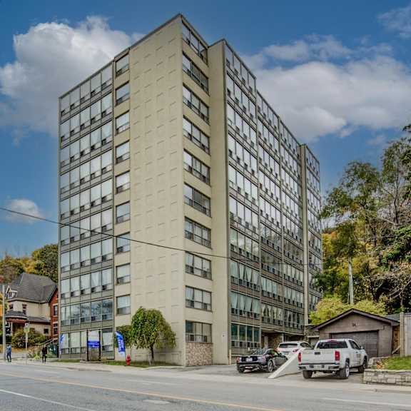 a tall beige building with many windows is surrounded by trees and parked cars.