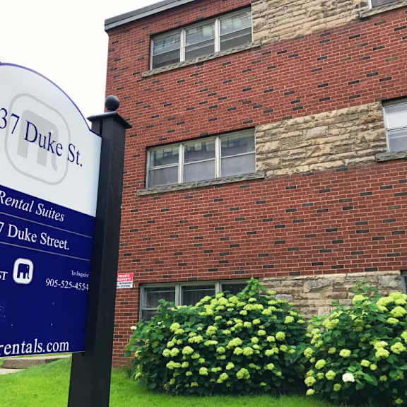 a sign for 137 duke st. rental suites stands in front of a brick building.
