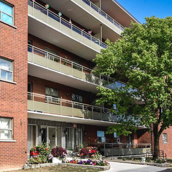 a red brick building with a balcony and a tree in front.