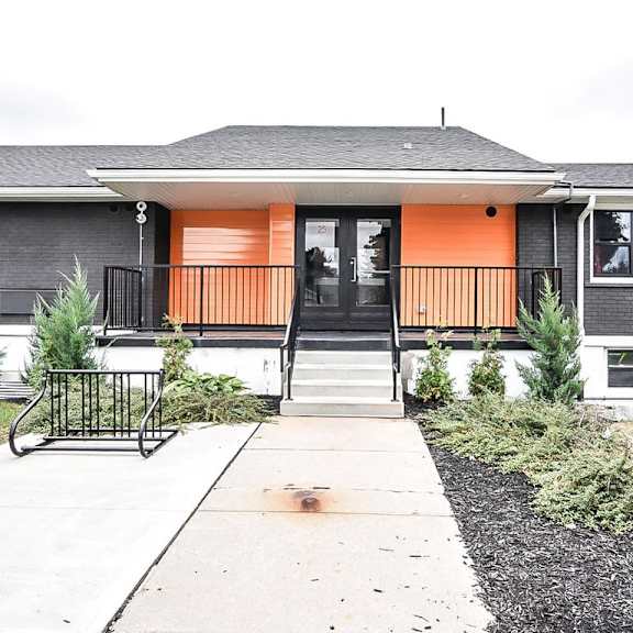 a grey house with an orange door and a black railing.