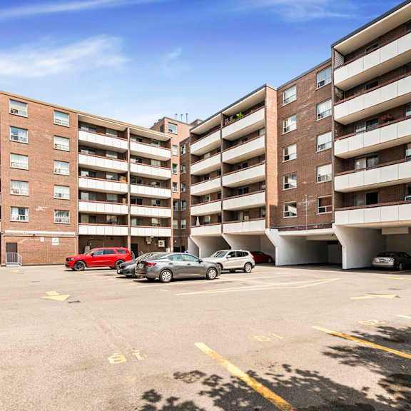 a parking lot in front of a multi-story apartment building with cars parked.