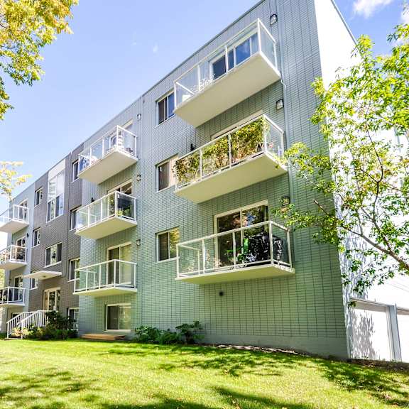a modern apartment building with balconies and green trees in the foreground.