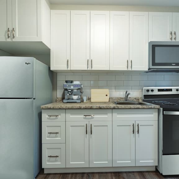 a kitchen with a refrigerator, microwave, oven, and cabinets.
