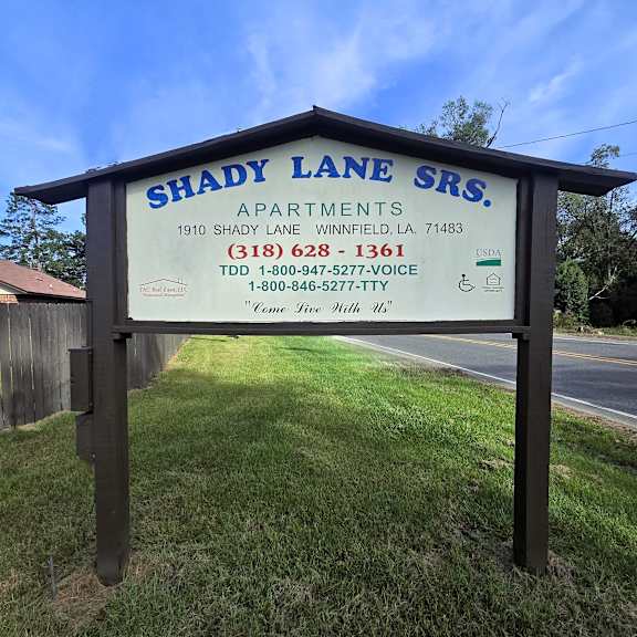a sign for shady lane srs apartments is displayed in front of a grassy area.