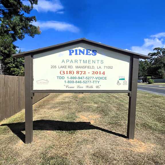 a sign for pines apartments with a phone number and address.