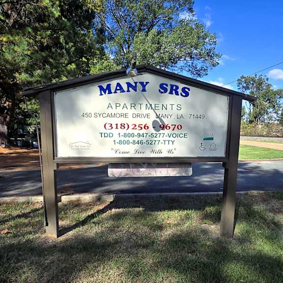 a sign for many srs apartments is displayed in front of a tree.