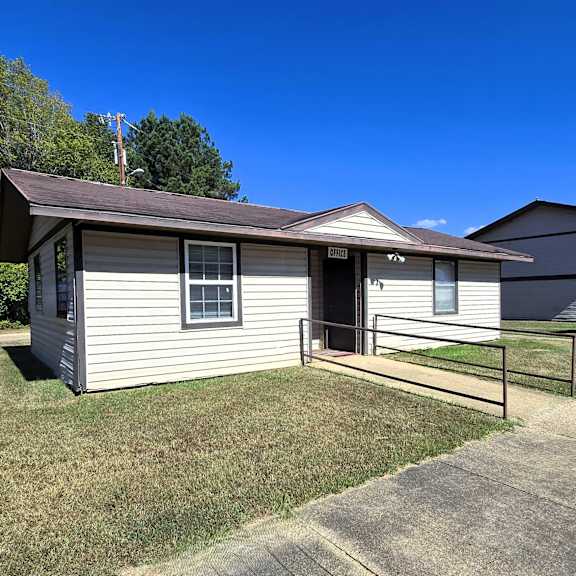 a small house with a brown roof and a grey siding is surrounded by a grassy lawn.