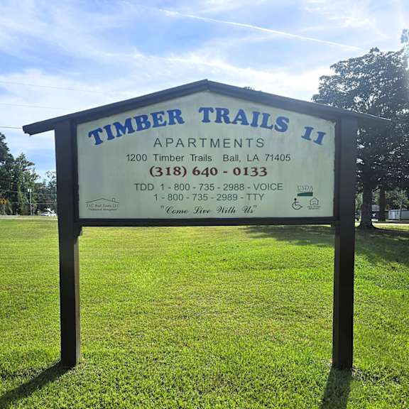 a sign for timber trails apartments stands in a grassy field.