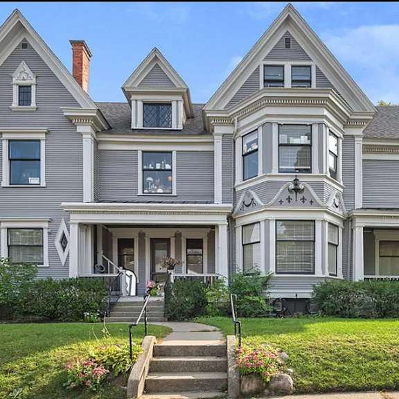 a large, grey victorian-style house with a front porch and a staircase leading to the entrance.