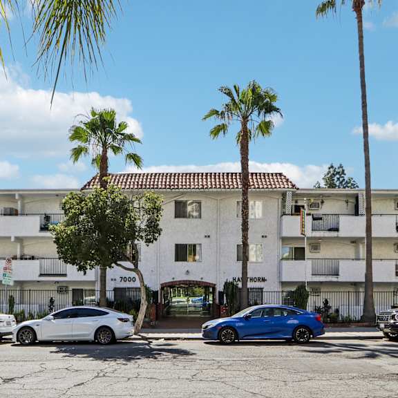 cars parked in front of a white apartment building with palm trees.