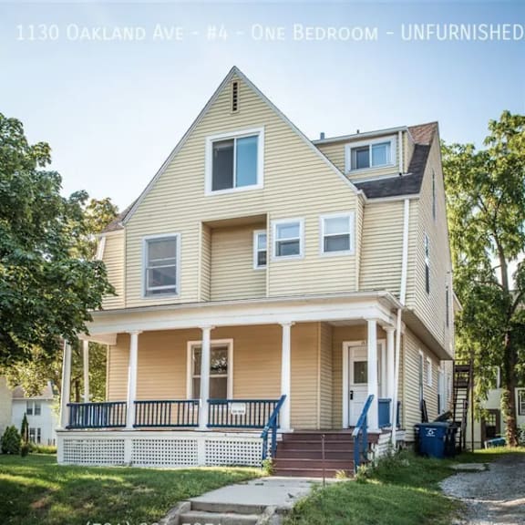 a two-story house with a porch and a blue trash can in front.