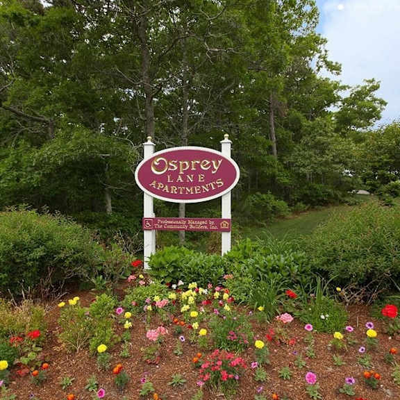 a sign for osprey landings apartments is surrounded by flowers.