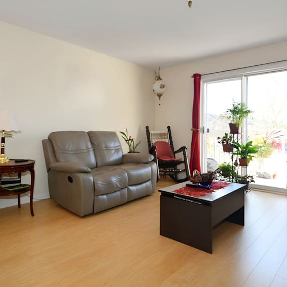 a living room with a grey leather sofa, a wooden side table with a lamp, a red chair, and a black coffee table.