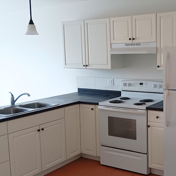 a white kitchen with a black counter top and white appliances.