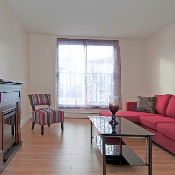 a living room with a red couch, a striped chair, and a wooden floor.