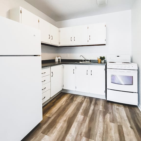a white kitchen with wood flooring and white appliances.