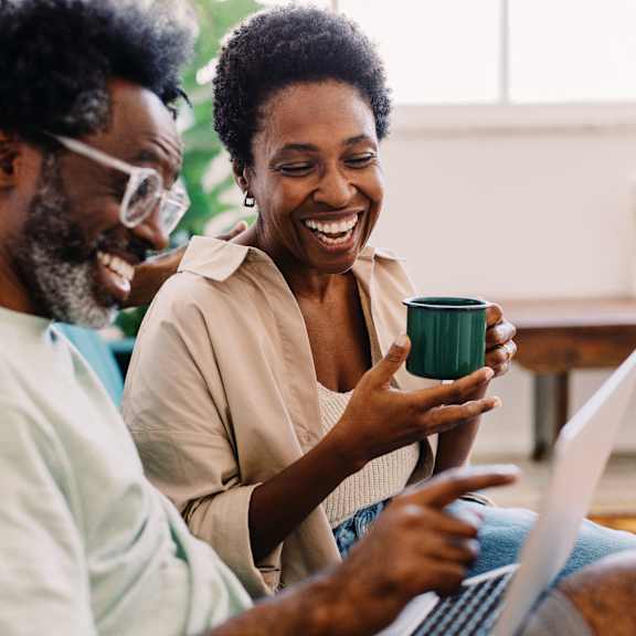 A man and a woman are laughing while looking at a laptop together.
