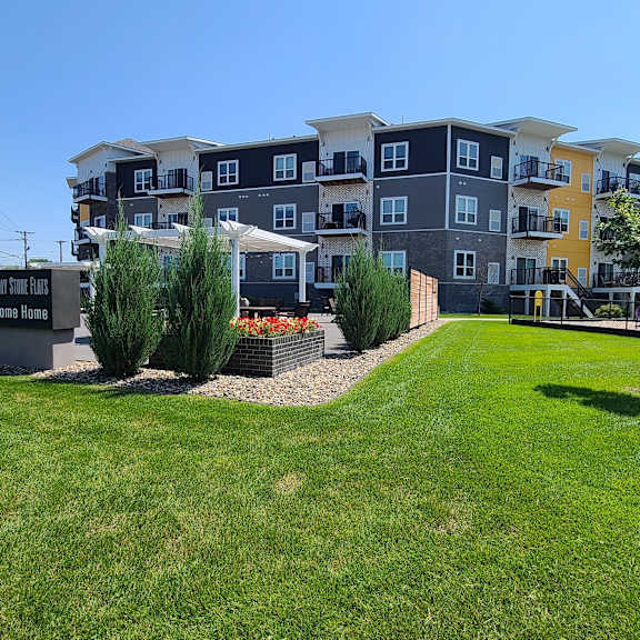 an apartment building with a green lawn and trees in front of it