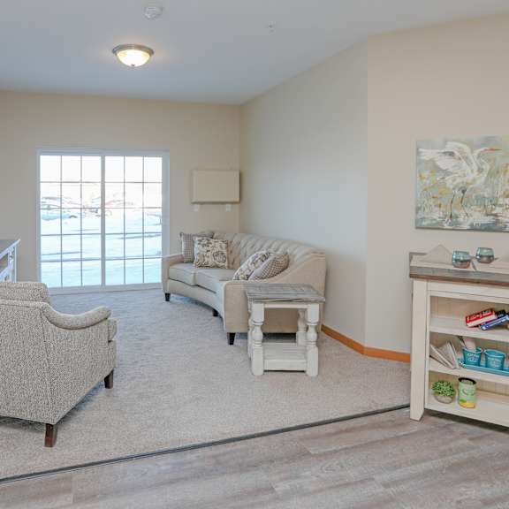 a living room with a grey sofa, a white chair and a wooden table with a painting on the wall.