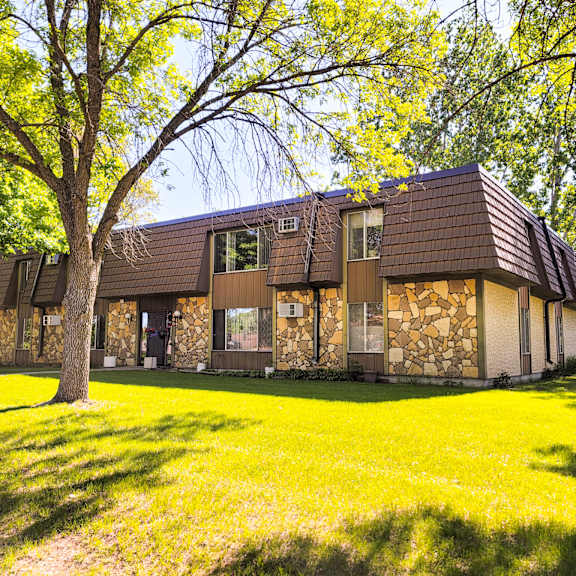 a house with a brown roof and a stone wall is surrounded by trees.