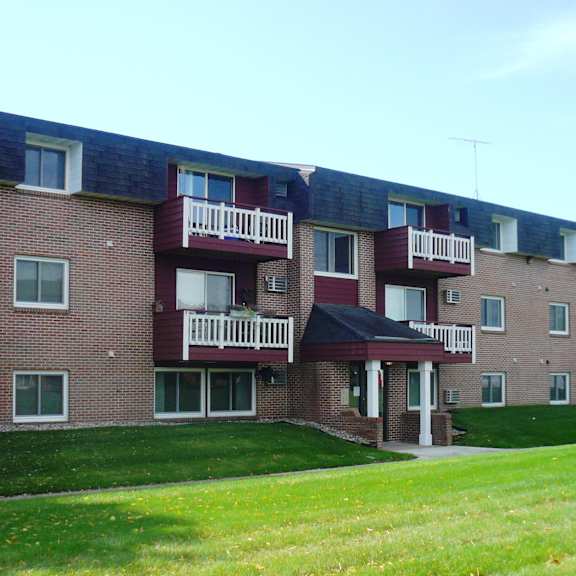 a red brick building with white balconies and a green lawn in front.