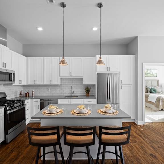 an l-shaped kitchen with a breakfast bar, two pendant lights, stainless steel appliances, hardwood-style flooring, and white cabinets.