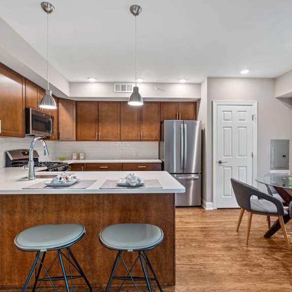 a kitchen with a breakfast bar, pendant and recessed lighting, and hardwood-style flooring near a dining room with a window.