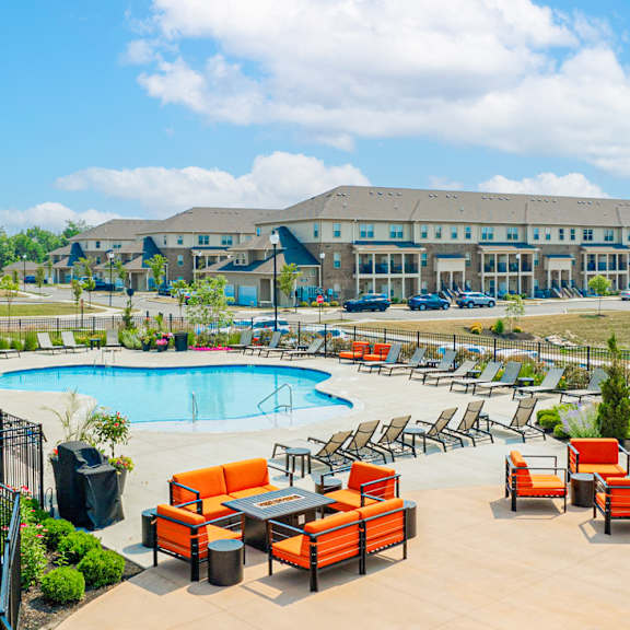 an outdoor pool with orange chairs and tables and a building in the background