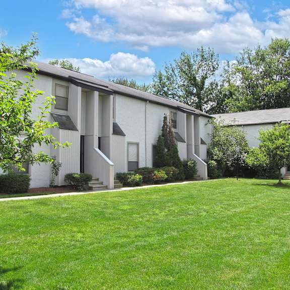 a white apartment building with a green lawn and trees