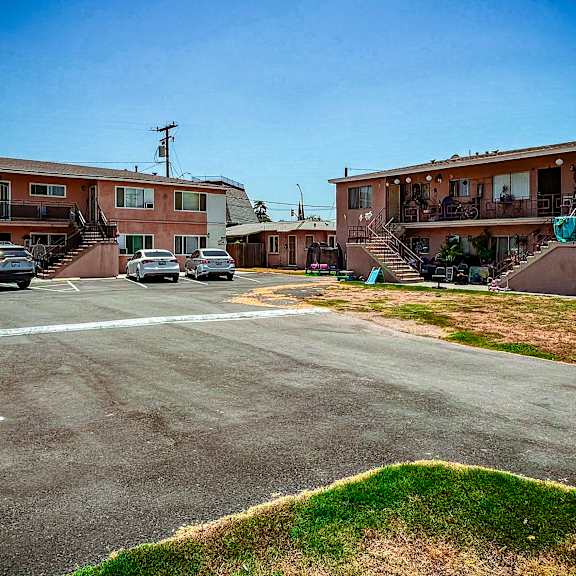 a parking lot in front of apartment buildings with cars parked.