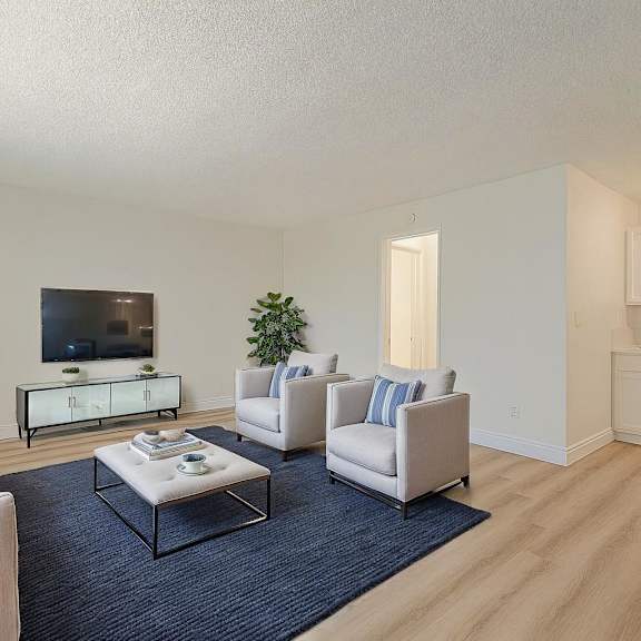 a living room with a white couch, a white chair, a black coffee table, and a television.