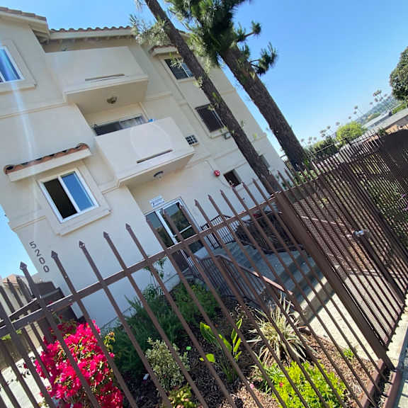 a tall white building with a balcony and a gate in front of it.