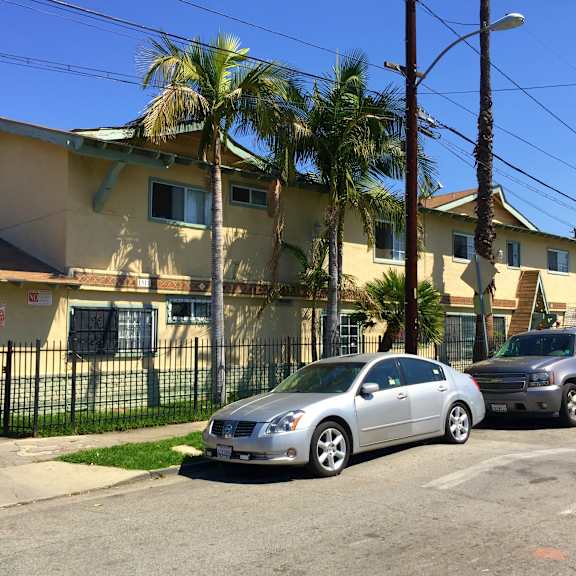 a silver car is parked in front of a yellow house with a black fence.