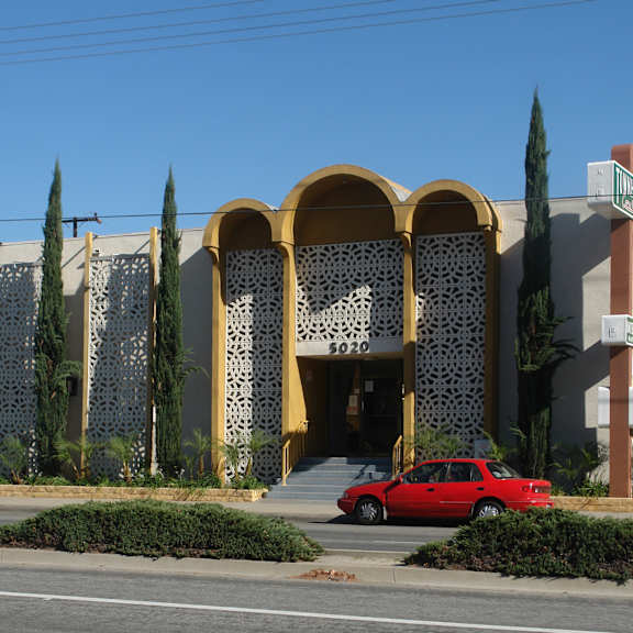 a red car is parked in front of a building with a yellow and white facade.