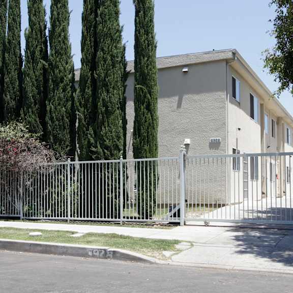 a house is surrounded by a tall fence and tall trees.