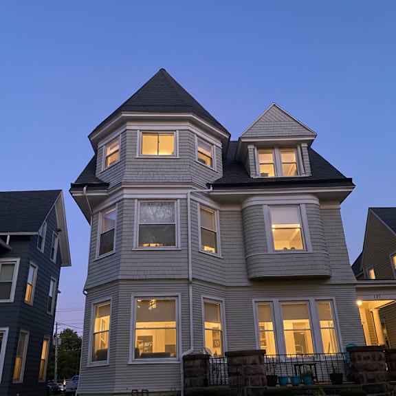 a large house with a tower and multiple windows is lit up at dusk.