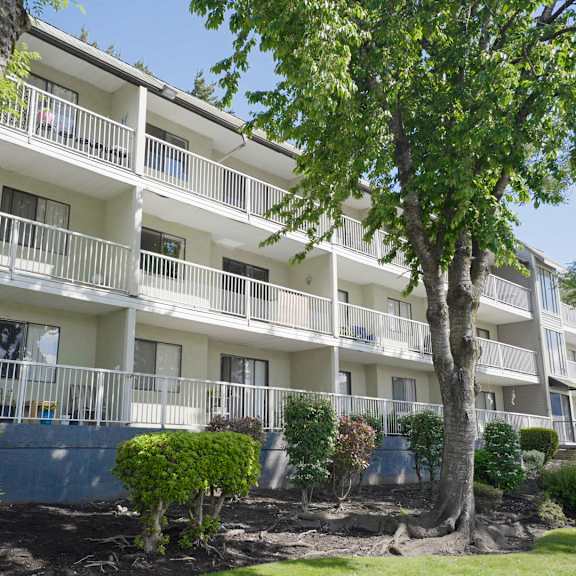 a white apartment building with balconies and trees in front.