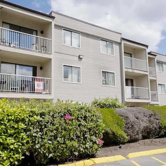 apartment building with balconies and bushes in front.